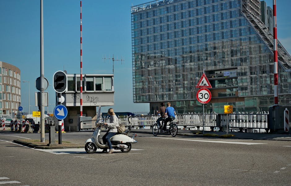 City street scene featuring scooter and bicycle riders near modern glass building.