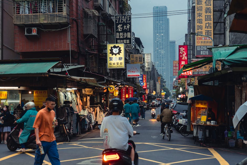 A vibrant street in Taipei bustling with people, scooters, and architecture.