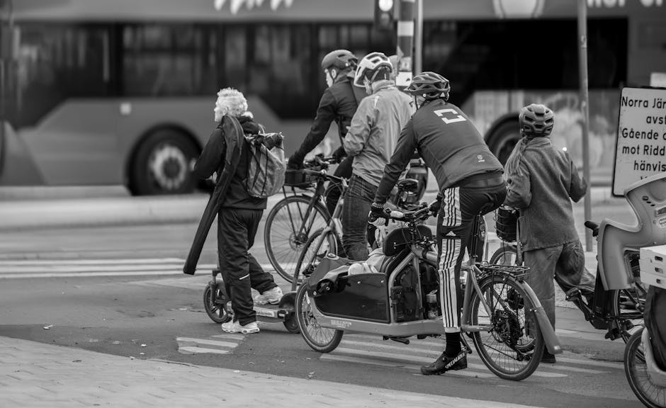 Black and white photo capturing cyclists and scooter riders waiting at a city intersection.