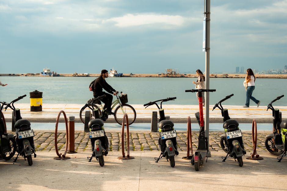 A cyclist rides along İzmir's scenic waterfront with parked scooters nearby under a cloudy sky.