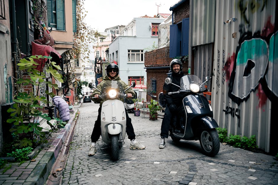 Two people on scooters enjoying a ride through a colorful urban alleyway filled with street art and plants.