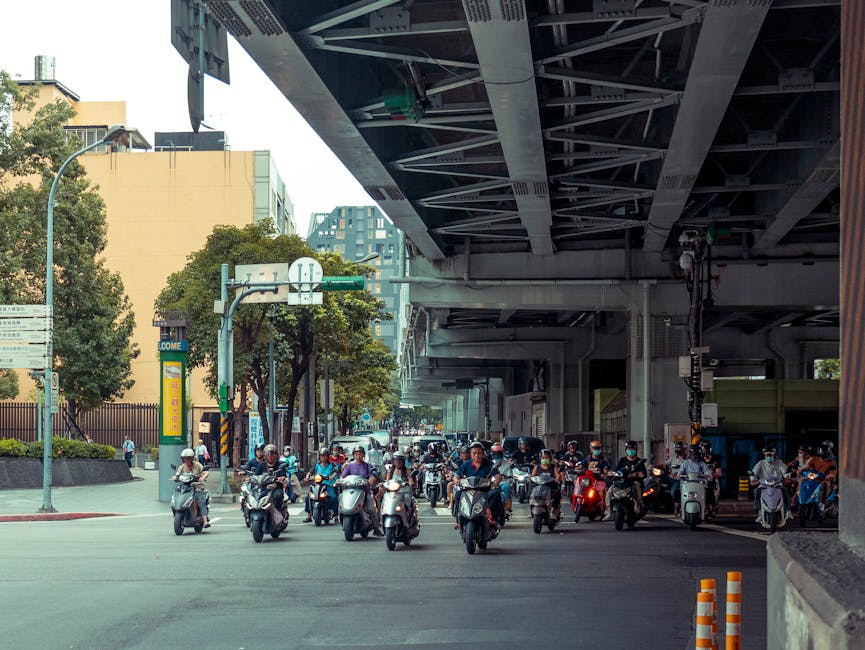Bustling city street scene with many motor scooters under a large overpass, capturing urban traffic.